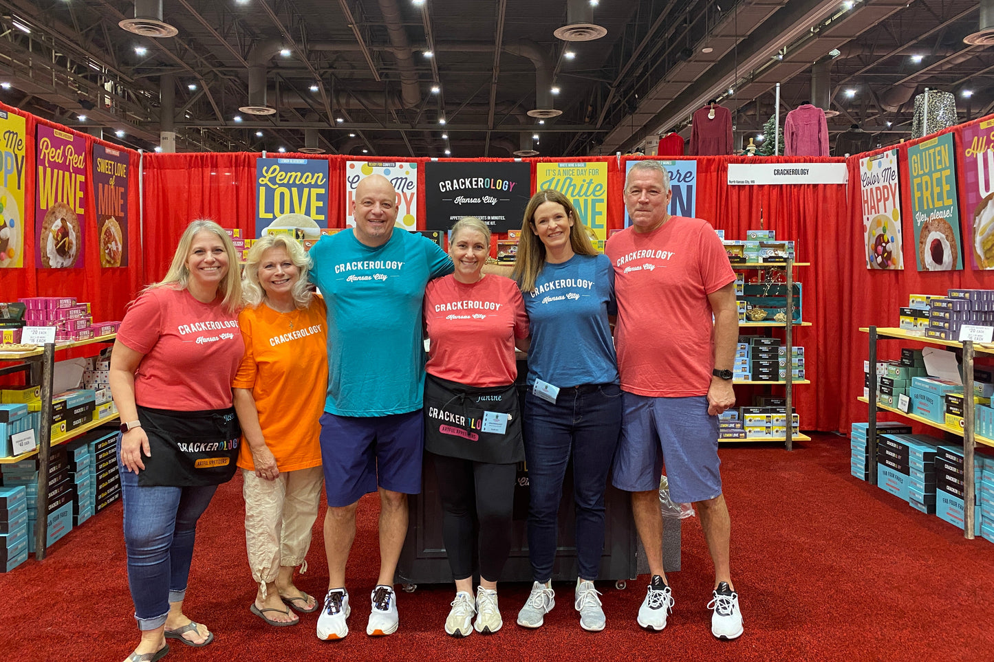 Group of people posing for a photo at a convention or trade show with booths in the background.