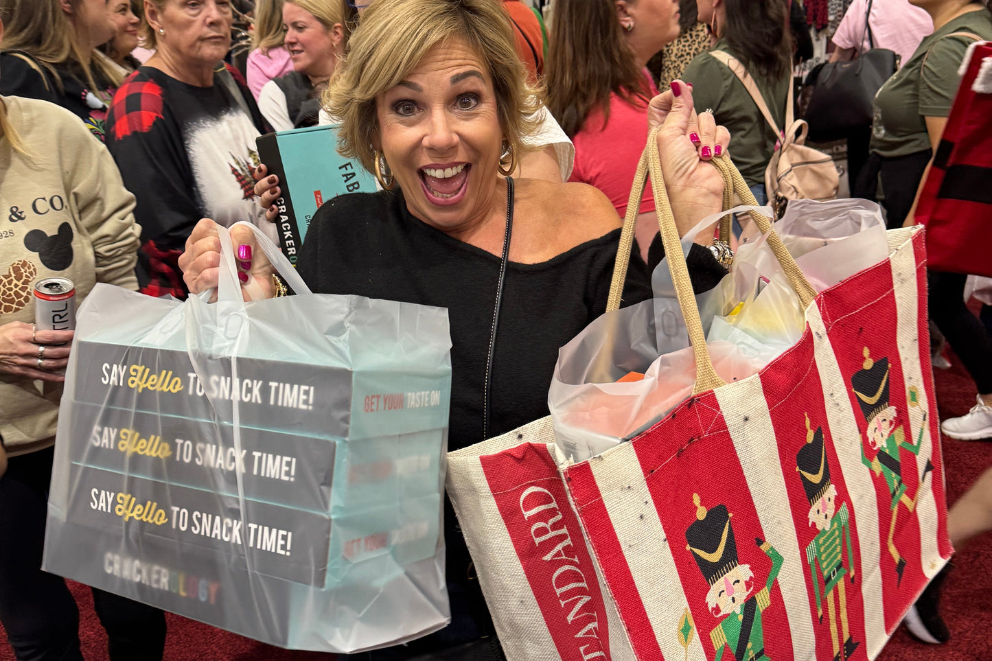 Woman holding a gift bag with a Christmas design in a crowded indoor setting.