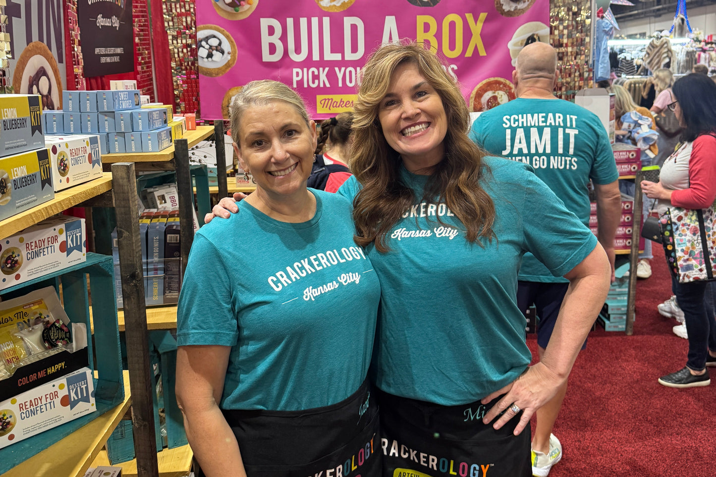 Two people wearing teal shirts with a Crackerology box in a store setting.
